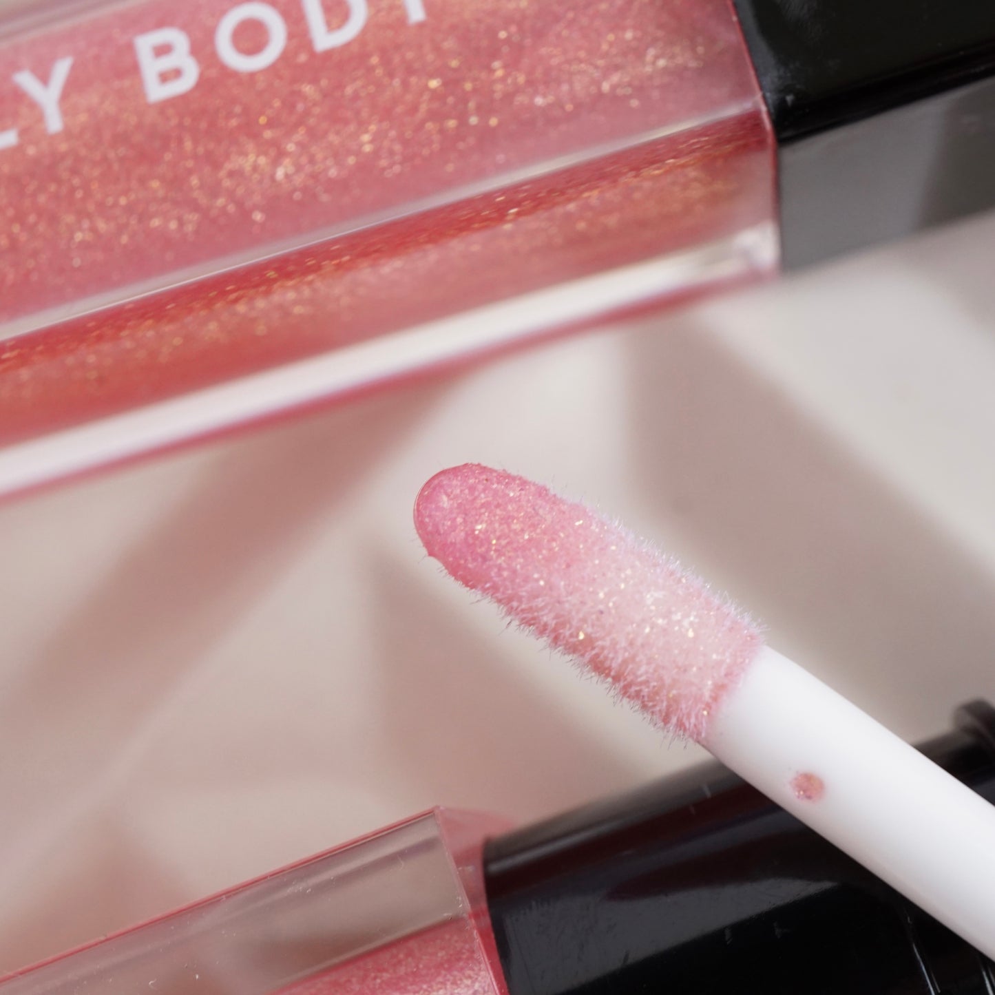 Close-up of a pink glittery lip gloss with applicator on a light background