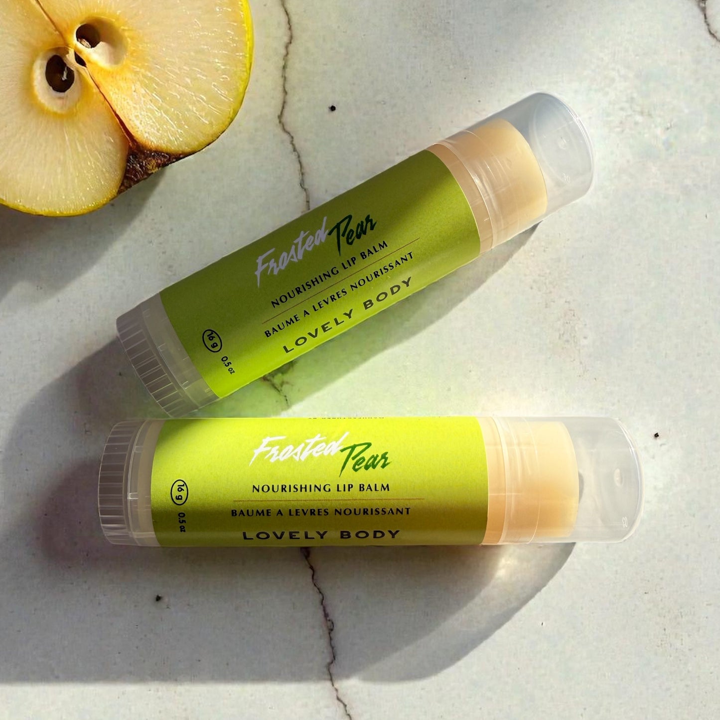 Two lip balms labeled 'Fruity Pear' on a marble surface with a halved pear.