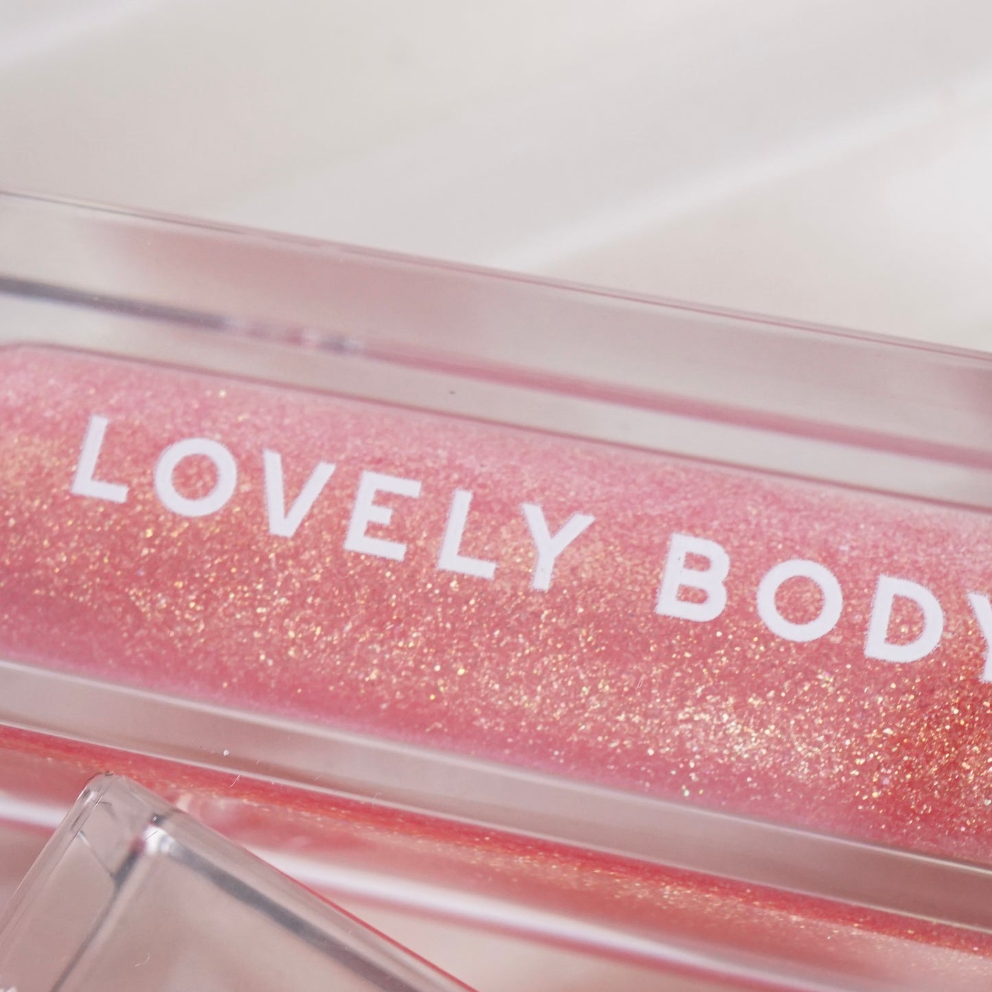 Pink glittery lip gloss with 'LOVELY BODY' text on a white background
