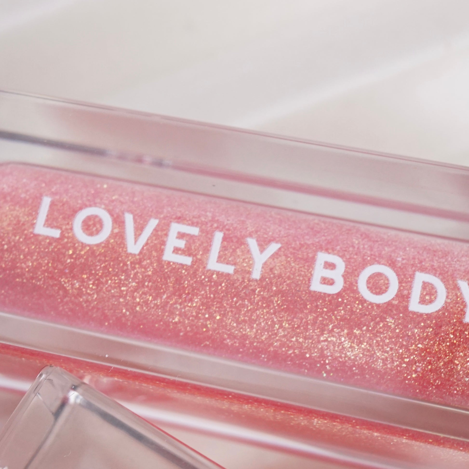 Pink glittery lip gloss with 'LOVELY BODY' text on a white background