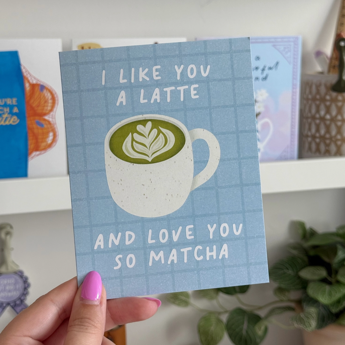 Card with a coffee cup illustration and text held by a hand on a shelf.