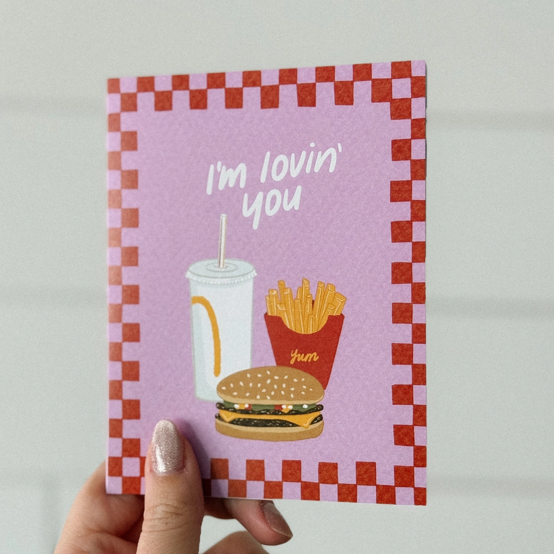 Card with a burger, fries, and drink illustration and 'I'm lovin' you' text on a checkered border.