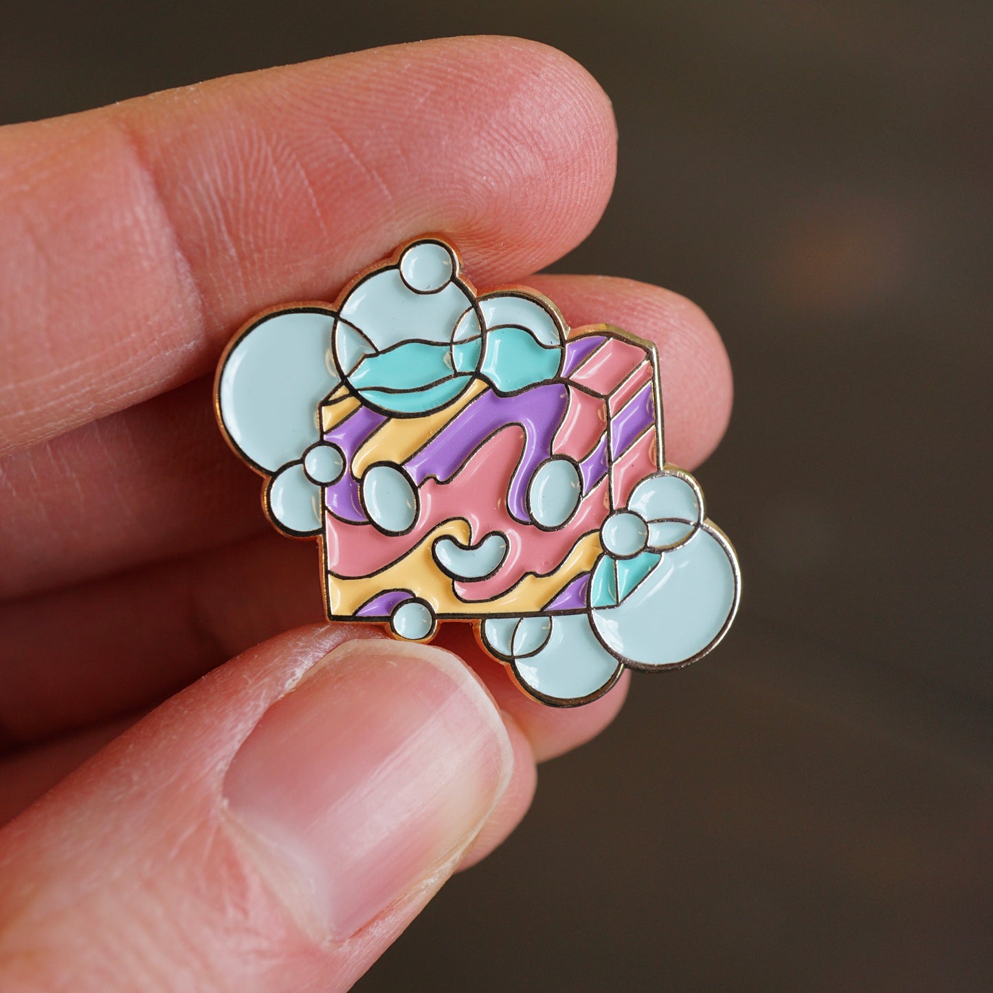 Small enamel pin of cartoon bar of soap in pink, blue, purple and yellow.