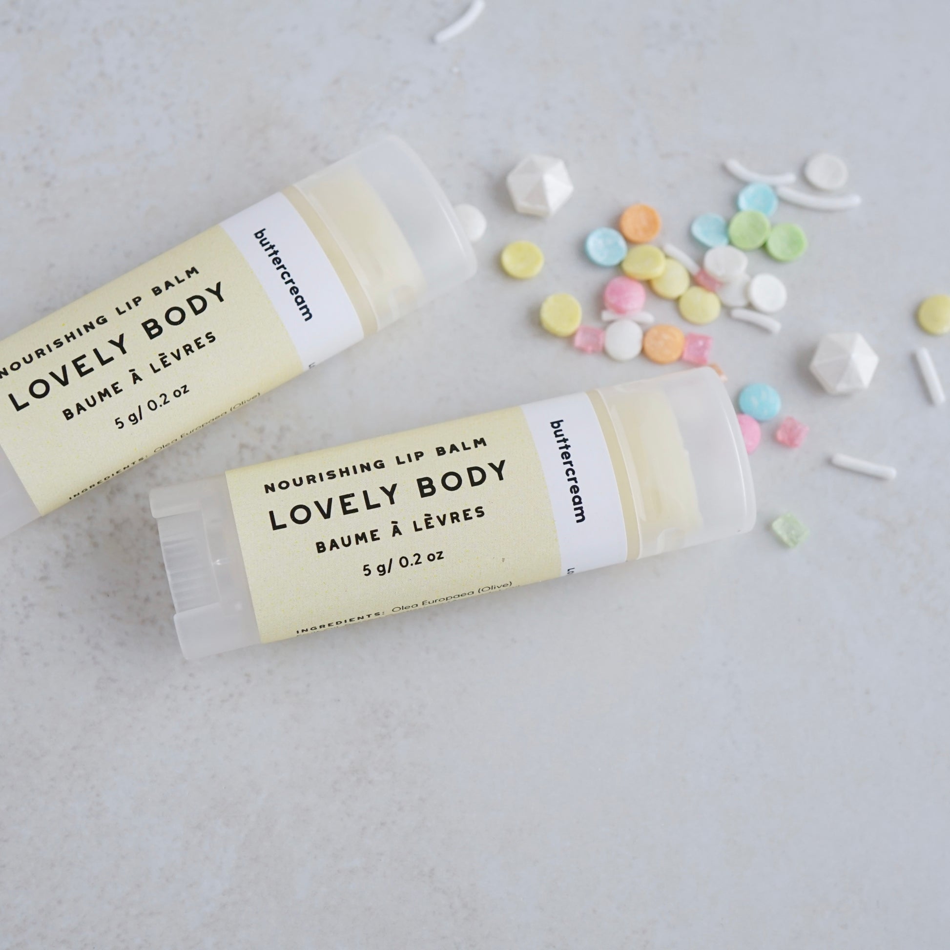 Two tubes of labelled lip balm next to small grouping of candy sprinkles for decoration.