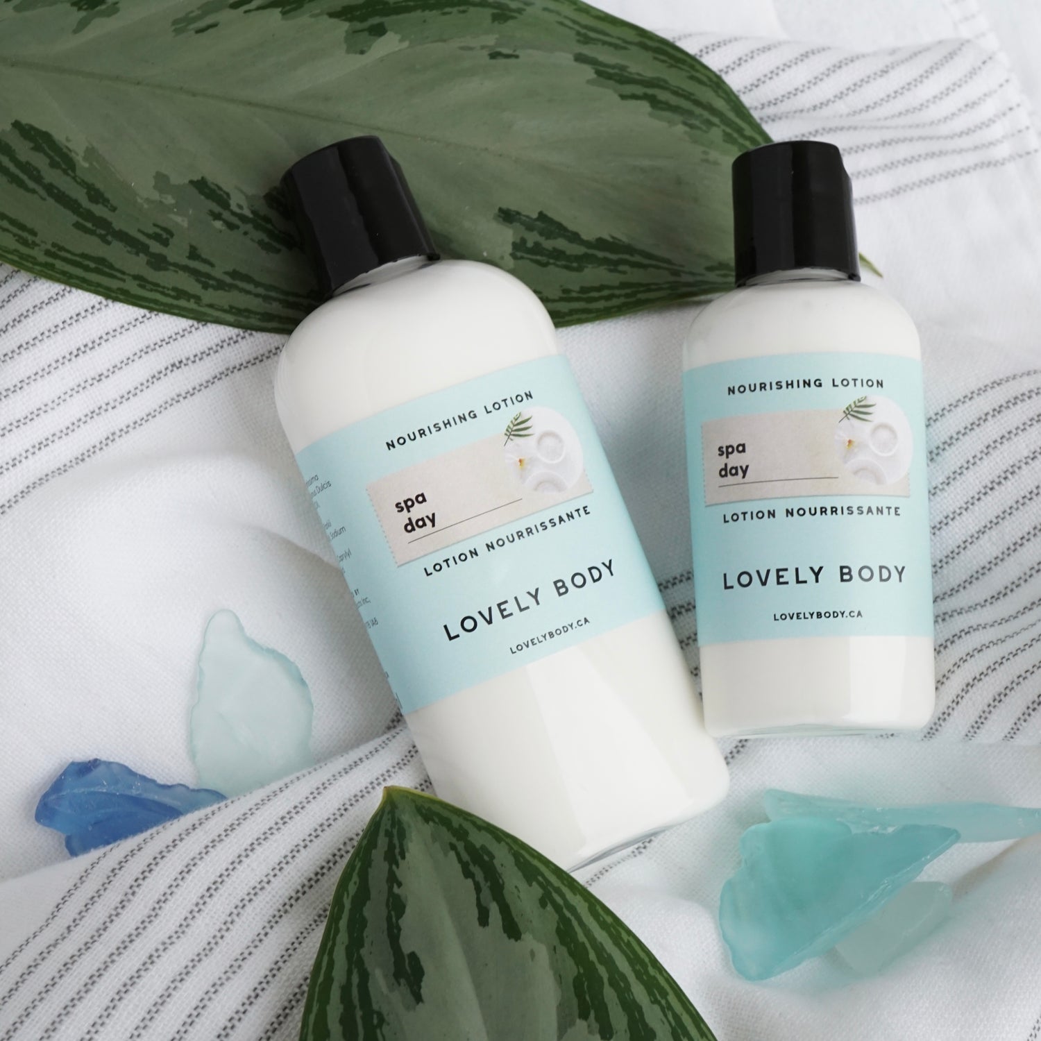 Two bottles of lotion on a towel with leaves and sea glass