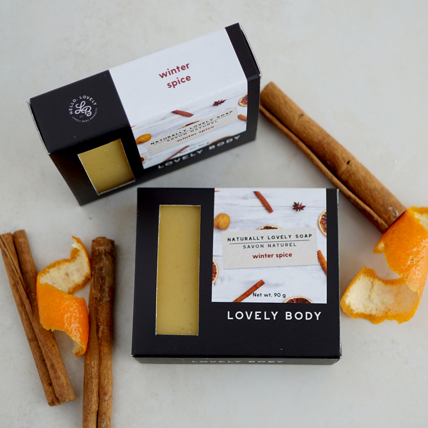 Two bars of soap in boxes surrounded by cinnamon sticks and orange peels