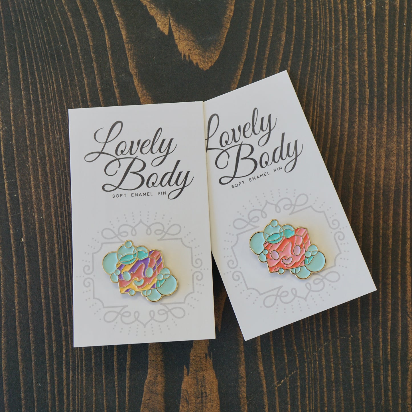 Two small enamel pins of a cartoon bar of soap on paper backing.