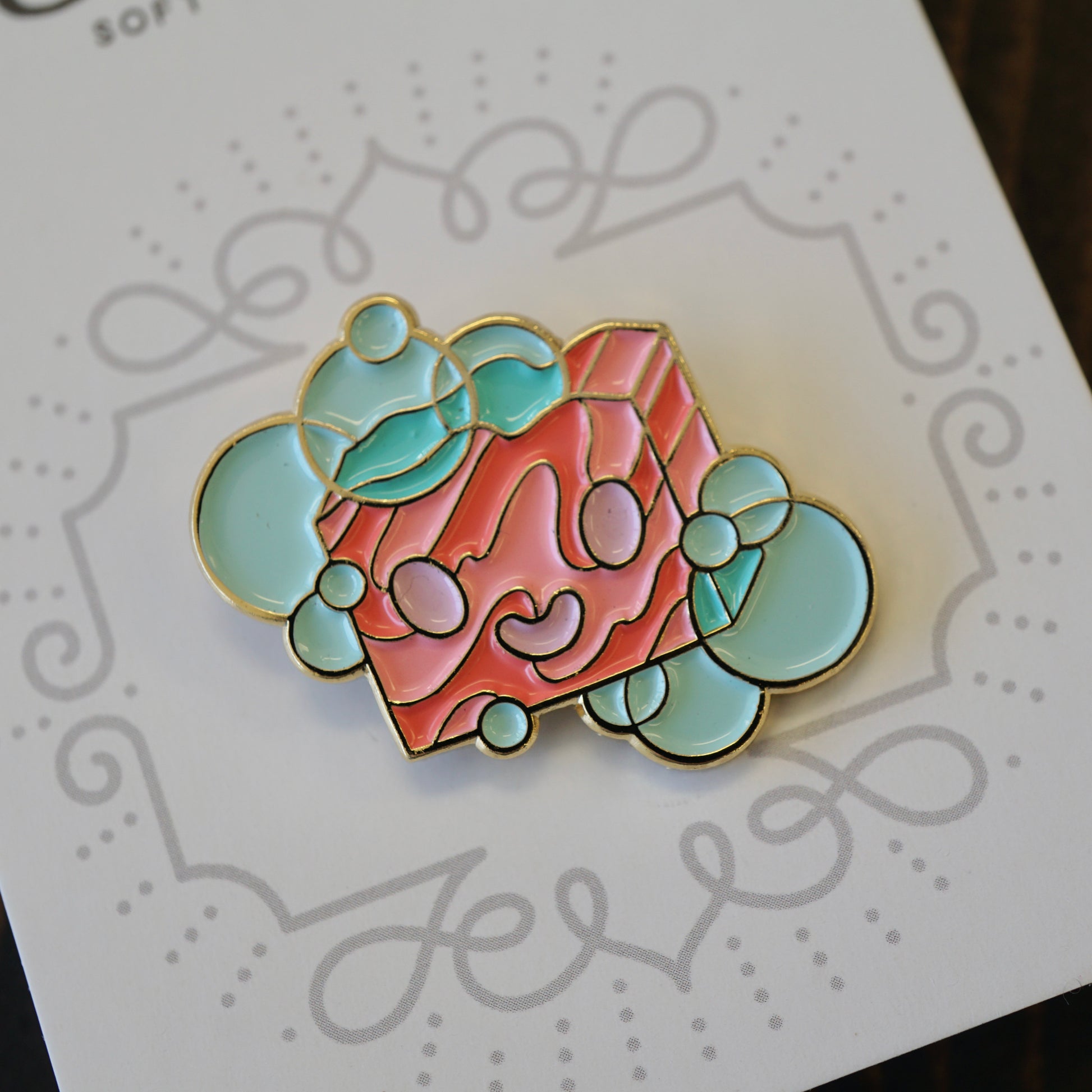 Small enamel pin of a cartoon bar of soap on paper backing.