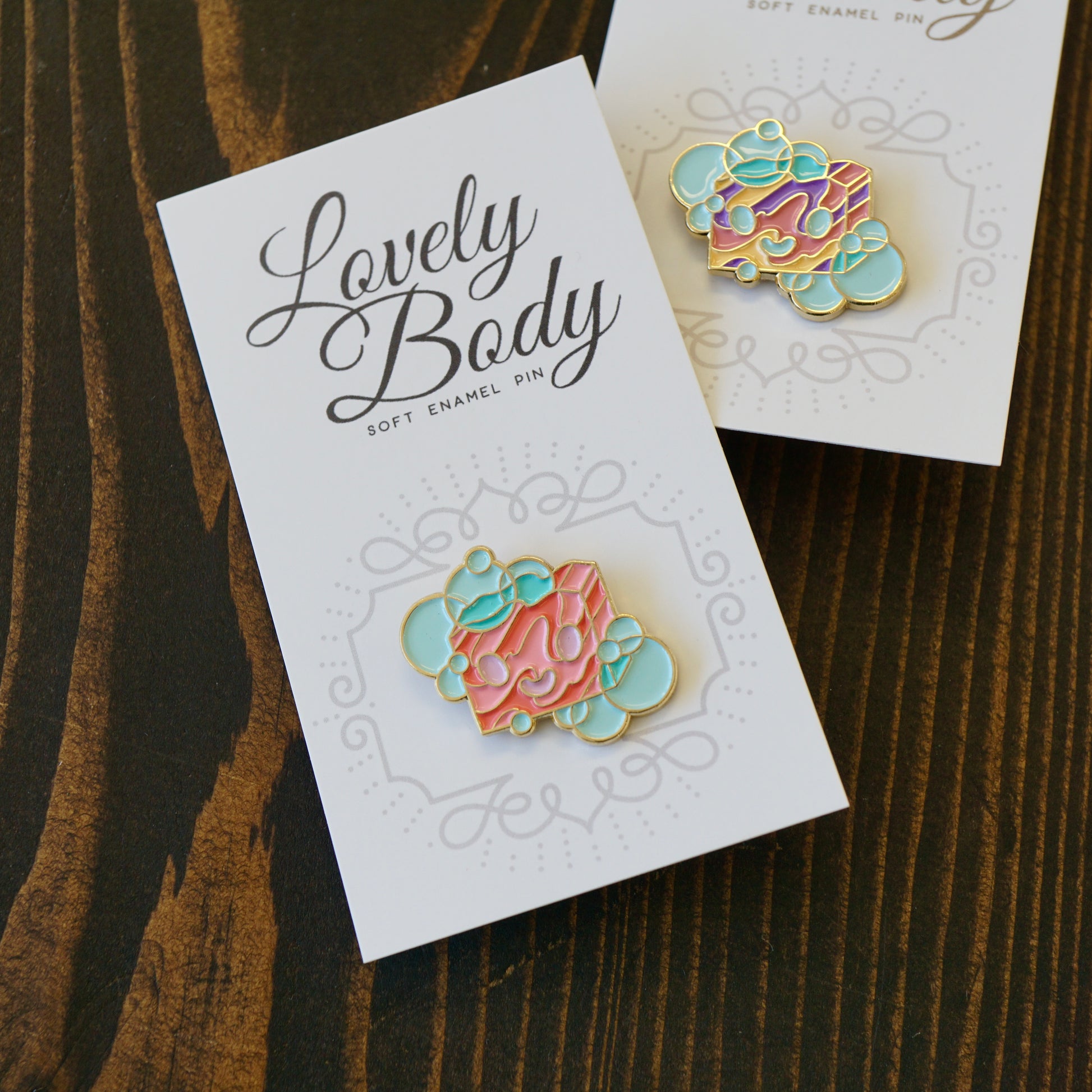 Two small enamel pins of a cartoon bar of soap on paper backing.